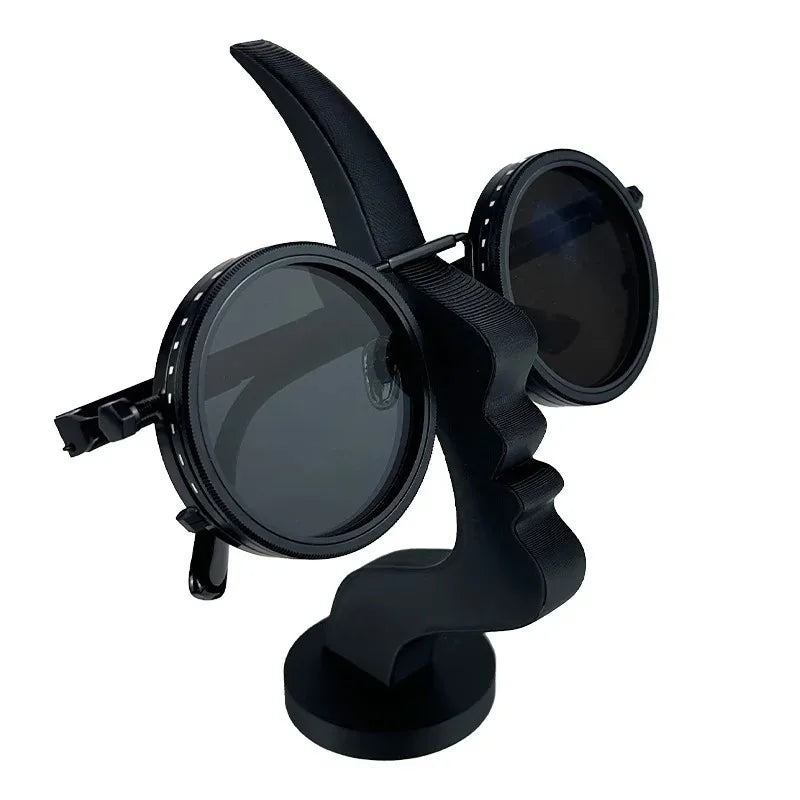 Black face-shaped glasses stand holding round sunglasses on a light-colored tabletop. 