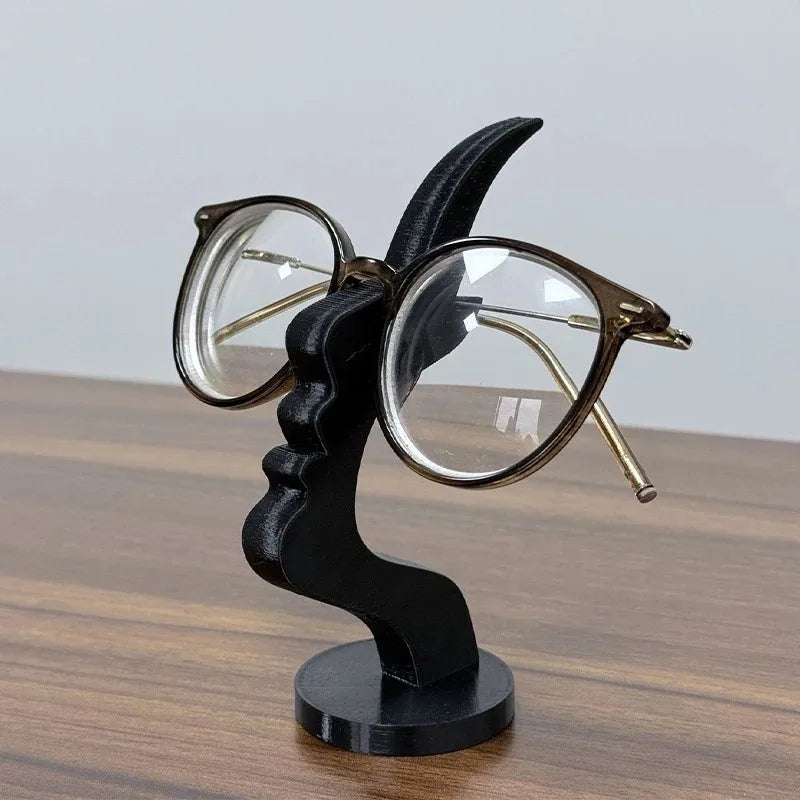 Black minimalist face eyeglass holder displaying round clear-frame glasses on a modern beige tabletop. 
