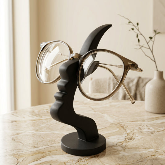Black minimalist face eyeglass holder displaying round clear-frame glasses on a modern beige tabletop. 